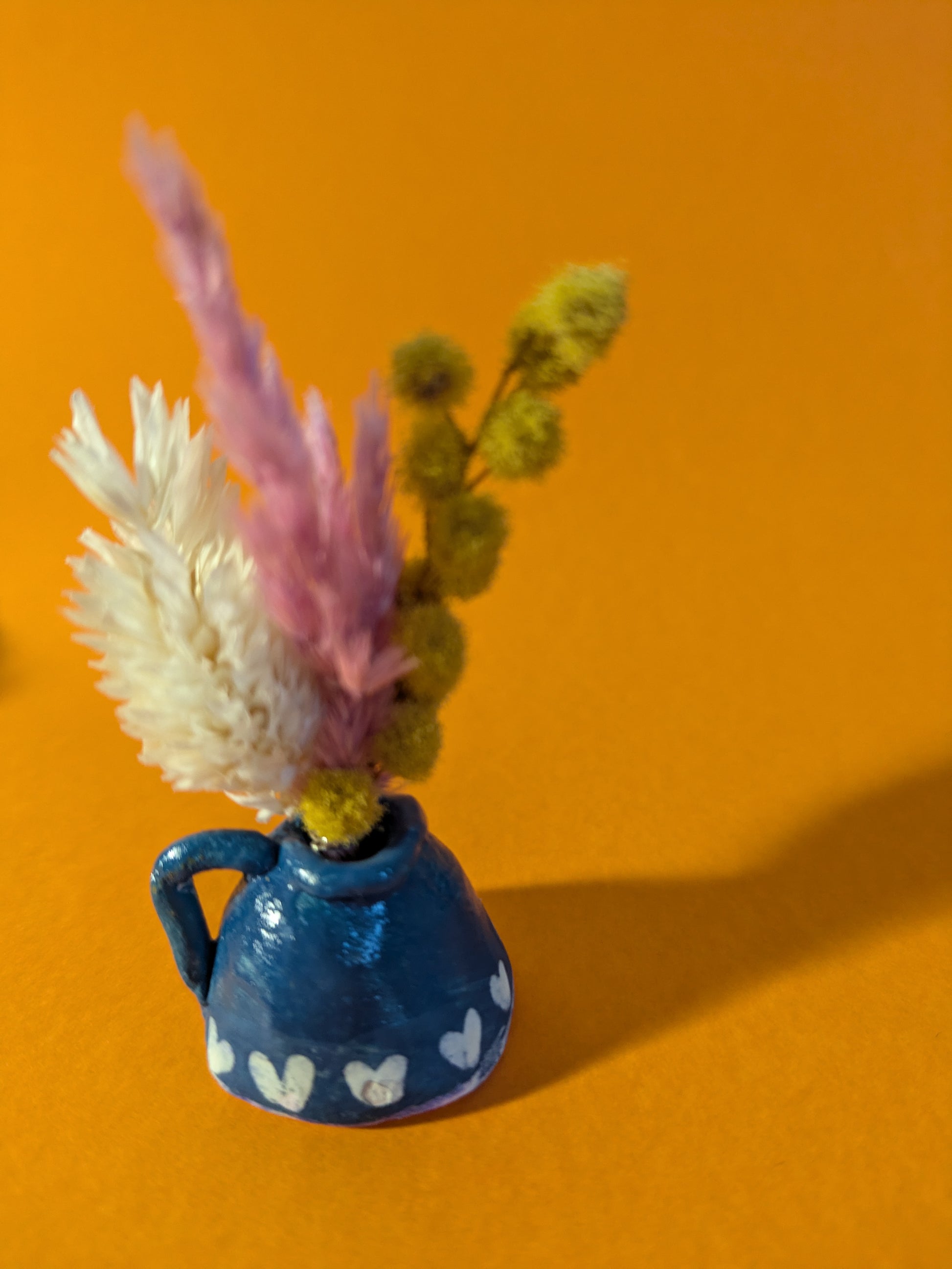 Mini vase en argile turquoise fait main avec un mini bouquet de fleurs séchées colorées. Accessoire de décoration bohème, idéal pour apporter une touche naturelle et originale aux petits espaces. Objet unique pour les amateurs de miniatures et de décoration poétique.