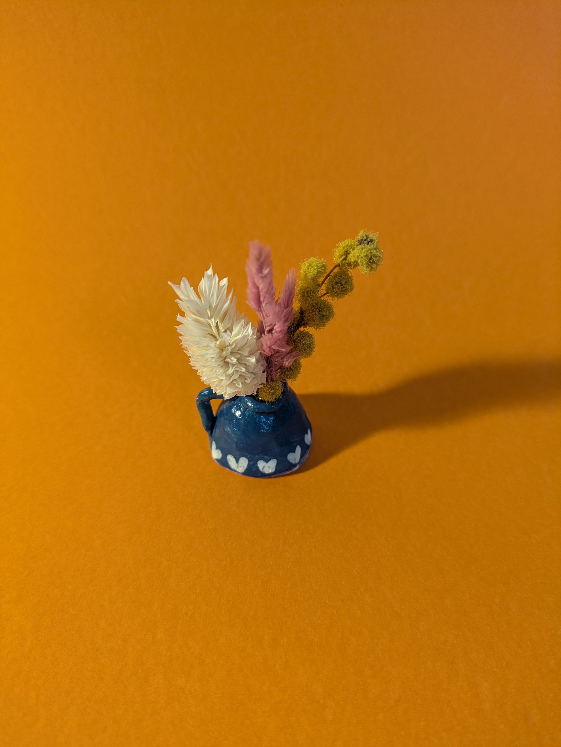 Mini vase en argile turquoise fait main avec un mini bouquet de fleurs séchées colorées. Accessoire de décoration bohème, idéal pour apporter une touche naturelle et originale aux petits espaces. Objet unique pour les amateurs de miniatures et de décoration poétique.